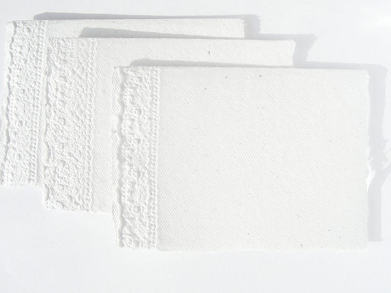 3 weiße Klappkarten aus handgeschöpftem Papier mit geprägtem Spitzenrand an einer Seite von paperuli liegen im Querformat fächerförmig auf dem Tisch.