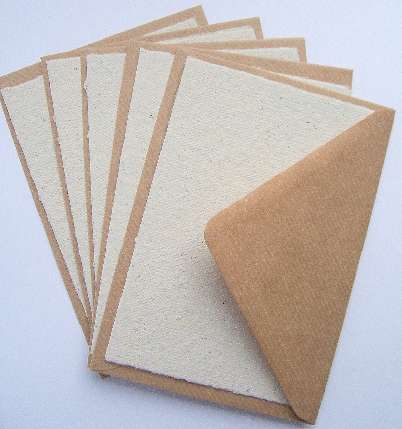 5 naturfarbene Klappkarten liegen jeweils in einen Kraftpapier-Umschlag geschoben fächerförmig auf dem Tisch.