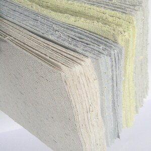 Ein ganzer Fächer handgeschöpfter Papiere in den 4 Farben Beige, Blau, Hellgrün und Hellgrau steht senkrecht im Querformat auf dem Tisch.