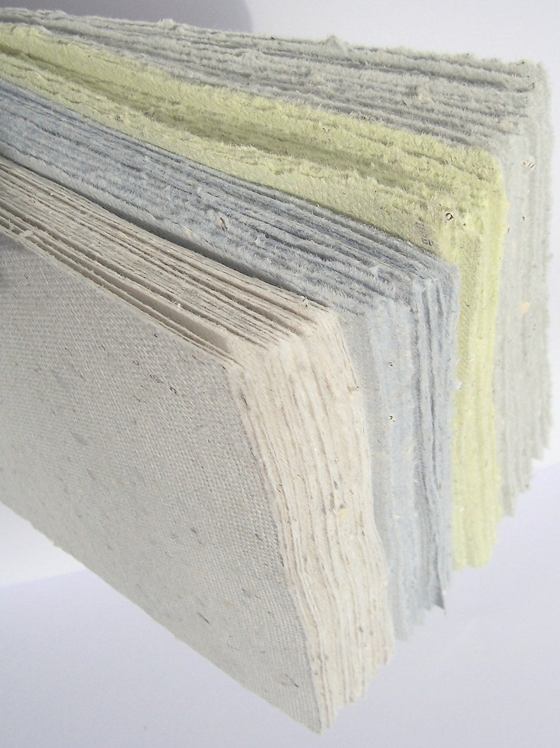 Ein ganzer Fächer handgeschöpfter Papiere in den 4 Farben Beige, Blau, Hellgrün und Hellgrau steht senkrecht im Querformat auf dem Tisch.