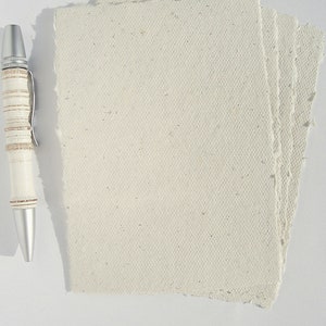 4 cremefarbene Büttenpapier-Postkarten liegen aufgefächert auf dem Tisch, links daneben ein Kugelschreiber zur Veranschaulichung der Größe.