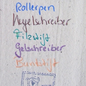 Weißer Büttenpapier-Zettel mit den Schriftproben einzelner Stifte.