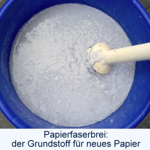 Blick in einen blauen Eimer, in dem ein Stabmixer weißen Papierbrei anrührt. Unter dem Foto steht der Text: "Papierfaserbrei: der Grundstoff für neues Papier".