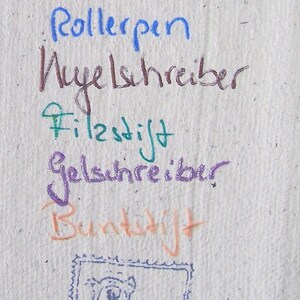 Foto des Schriftprobenzettels. Mit verschiedenen Stiften ist jeweils geschrieben worden (von oben nach unten): "Füller/Tinte", "Rollerpen", "Kugelschreiber", "Filzstift", "Gelschreiber", "Buntstift". Unten ist ein Stempelabdruck zu sehen mit dem Motiv einer quadratischen Briefmarke mit Zackenrand, auf der ein Bär einen Briefumschlag in der ausgestreckten Hand hält.