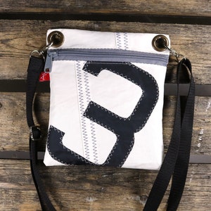 Puede incluir: Un bolso bandolera blanco con un diseño en blanco y negro. El bolso tiene cierre de cremallera y una correa ajustable negra.