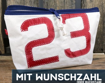 May include: White canvas zippered pouch with a red number "23" sewn on the front. The text "MIT WUNSCHZAHL ODER BUCHSTABE" is printed below the pouch.