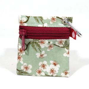 Puede incluir: Pequeño monedero cuadrado con estampado floral. La tela es verde claro con flores blancas y centros marrones. Tiene una cremallera burdeos y un clip de metal plateado. El monedero mide aproximadamente 7,6 cm de ancho y 7,6 cm de alto.