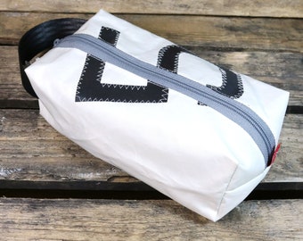 May include: White zippered pouch with a black "L" design. The pouch is made of a canvas-like material and has a gray zipper.
