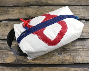 May include: White canvas zippered pouch with a red and white nautical knot design. The pouch has a black carrying handle.