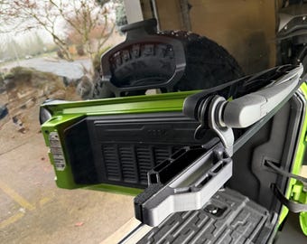 Könnte beinhalten: Nahaufnahme einer limettengrünen Jeep-Ladefläche mit einer schwarzen, strukturierten Oberfläche. Ein schwarzes und graues Zubehör ist an der Ladefläche befestigt. Das Jeep-Logo ist auf der Seite der Ladefläche sichtbar.
