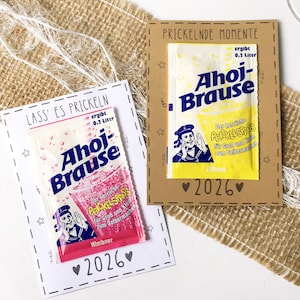 Könnte beinhalten: Zwei Karten mit Ahoj-Brause-Getränkepäckchen. Eine Karte trägt die Aufschrift "LASS ES PRICKELN" mit einem rosa Päckchen, die andere "PRICKELNDE MOMENTE" mit einem gelben Päckchen. Beide Karten haben "2026" und Stern- und Herzdekorationen. Die Päckchen zeigen eine Seemannsgrafik.
