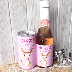 Peut inclure: Une canette et une bouteille roses de Froh-Secco avec un motif de cerf. La canette et la bouteille ont une étiquette blanche et rose avec le texte "Froh-Secco" et "Für dich". La bouteille est remplie d'un liquide rose.
