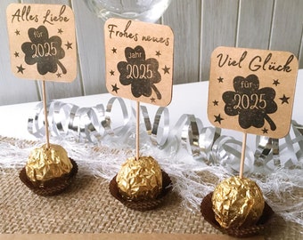 May include: Three chocolate truffles with brown paper flags. The flags have the text "Alles Liebe für 2025", "Frohes neues Jahr 2025", and "Viel Glück für 2025".