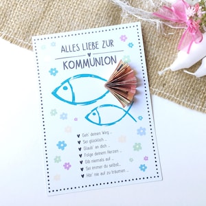 Op de afbeelding: Een communiekaart met een blauw visontwerp en de tekst "Alles Liebe zur Kommunion". De kaart is versierd met een waaier van gevouwen bankbiljetten. De achtergrond omvat witte kaarsen, bloemen en jute.
