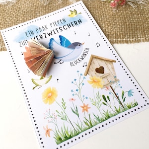 May include: A white card with a blue bird holding money in its beak. The card has a birdhouse, flowers, and the text "Ein paar piepen zum verzitschern" and "Gl&uuml;ckwunsch".