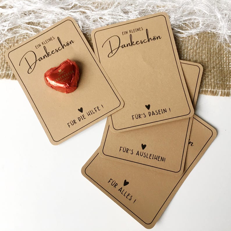 May include: Four brown cardstock gift tags with the text "Ein kleines Dankesch&ouml;n" and different messages of thanks. The top tag has a small red heart-shaped chocolate on it.