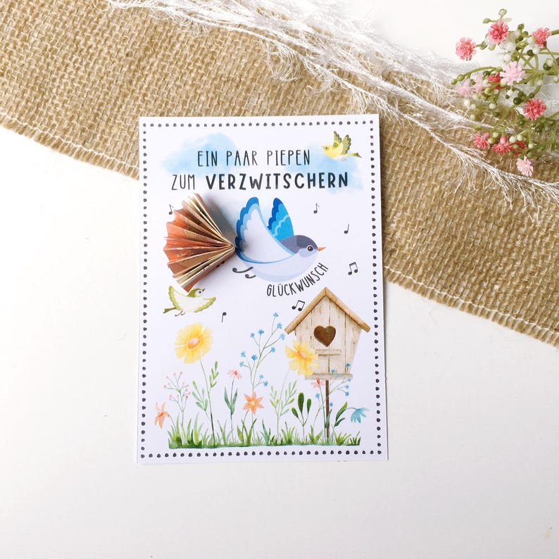 May include: A white card with a blue bird illustration and the text "Ein paar piepen zum verzwitchern" and "Gl&uuml;ckwunsch". The card has a pop-up bird with brown wings and a yellow birdhouse with a heart.