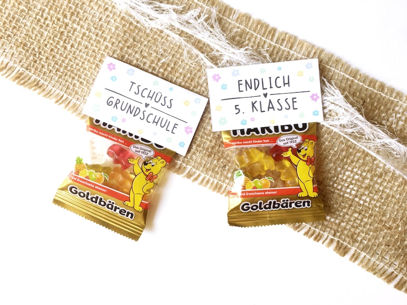 May include: Two small bags of gummy bears with decorative labels. One label reads "Tsch&uuml;ss Grundschule" and the other says "Endlich 5. Klasse". The gummy bear bags are gold and feature a cartoon bear.