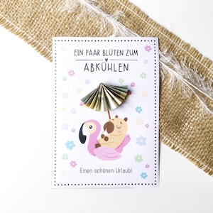 以下が含まれることがあります： 「Ein paar Blüten zum Abkühlen」と「Einen schönen Urlaub！」のテキストが入ったグリーティングカード。ピンクの浮き輪に乗った漫画のフラミンゴとカピバラが描かれています。紙の傘が日陰を作っています。カードは小さな花で飾られています。