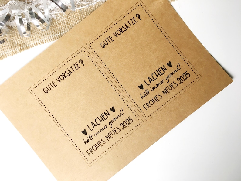 Pu&ograve; includere: Due carte di carta marrone con testo nero. Il testo sulle carte dice "Gute Vors&auml;tze?" e "&hearts; Lachen h&auml;lt immer gesund! Frohes Neues 2025".