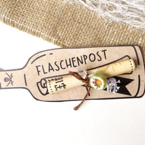 May include: A brown paper bottle with a rolled up scroll inside. The bottle has the text "FLASCHENPOST" written on it. The scroll is tied with twine and has a small candy on it.