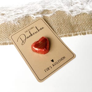 May include: A small brown card with the text "Ein kleines Dankesch&ouml;n" and a heart-shaped chocolate. The card also has the text "F&uuml;r's Ausleihen!" on the bottom.
