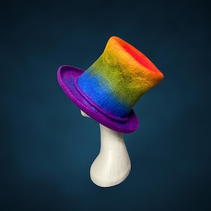 Pode incluir: Um chapéu de copa arco-íris com aba roxa e um suporte branco. O chapéu transita do vermelho para o laranja, amarelo e verde, depois para o azul e roxo. O chapéu é exibido em um fundo azul escuro.