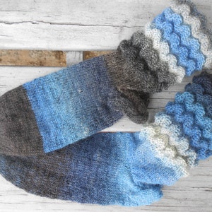 Pode incluir: Um par de meias de malha feitas à mão em tons de azul, cinza e castanho. As meias apresentam um padrão de cores gradiente e uma bainha decorativa com babados. As meias são feitas de fio macio.