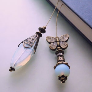 Könnte beinhalten: Zwei zarte Lesezeichen mit Opal-Glasperlen und bronzenen Akzenten. Ein Lesezeichen zeigt einen Schmetterlingsanhänger, während das andere ein filigraneres Design hat.