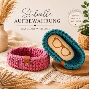 Könnte beinhalten: Zwei ovale Häkelkörbe in Magenta und Petrol mit Holzboden und kleinem braunen Lederetikett. Der petrolfarbene Korb hat ein eingraviertes Brillensymbol auf dem Holzboden. Der Text lautet Stilvolle Aufbewahrung, Handmade with Love und Stilvoll Praktisch Nachhaltig.