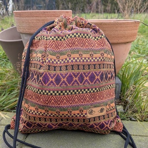 Può includere: Una borsa a sacco con un motivo geometrico colorato in tonalità di arancione, rosso, viola, verde e nero. La borsa ha laccetti neri.