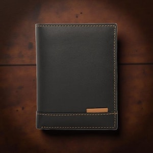 Könnte beinhalten: Eine schwarze Lederbrieftasche mit beigen Nähten und einem kleinen beigen Akzent. Die Brieftasche ist rechteckig und scheint zweifach gefaltet zu sein. Die Nähte sind an den Rändern und am Akzent sichtbar.