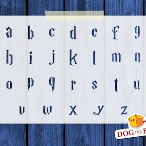 May include: A white stencil with the lowercase alphabet in a gothic font. The letters are dark blue and are arranged in rows. The stencil is taped to a blue wooden surface. The logo "DOG IN A BOX" is in the bottom right corner.
