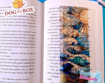 May include: A rectangular bookmark with a stained glass design featuring a sun, clouds, and ocean waves in shades of blue, orange, and white. The bookmark is placed in an open book. The text "Crystal Bookmarks" is visible.