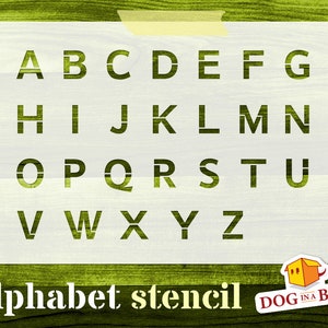 May include: White alphabet stencil featuring the letters A to Z in a simple, blocky font. The stencil is set against a green wood background. The text "Alphabet stencil" is below the stencil, and a logo for "DOG IN A BOX" is in the bottom right corner.
