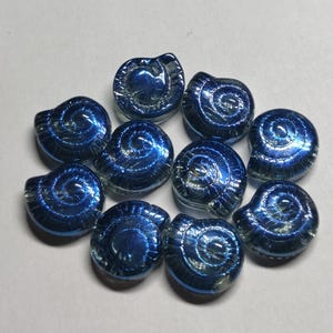 Könnte beinhalten: Zehn schimmernde blaue Glasschneckenhäuser mit einem Spiraldesign. Die Muscheln sind glatt und haben eine glänzende Oberfläche.