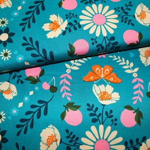 Könnte beinhalten: Türkiser Stoff mit einem sich wiederholenden Muster aus weißen Blumen, rosa Kreisen, orangefarbenen Schmetterlingen und dunkelblauen Blättern.