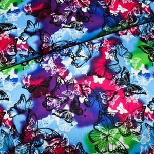 Könnte beinhalten: Ein farbenfroher Stoff mit einem sich wiederholenden Muster aus schwarzen Schmetterlingen auf einem Hintergrund aus Blau, Lila, Rosa und Grün. Die Schmetterlinge sind in verschiedenen Größen und Positionen angeordnet und erzeugen ein dynamisches und lebendiges Design.