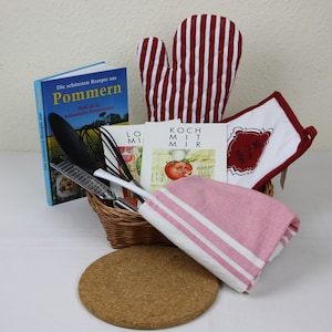 Puede incluir: Una cesta de regalo con temática de cocina con un guante de cocina a rayas rojas y blancas, un salvamanteles a juego, una toalla a rayas rosas y blancas, libros de cocina y utensilios de cocina. Incluye un salvamanteles de corcho y una cesta de mimbre.