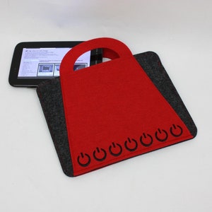 Op de afbeelding: Rode tablet-hoes van vilt met een zwarte viltbies en een handvat. De hoes heeft een rij stroomknopsymbolen langs de onderkant.