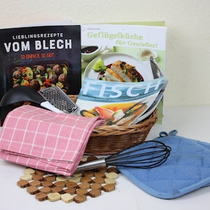 Puede incluir: Una cesta de mimbre llena de artículos de cocina, incluyendo dos libros de cocina, una toalla de cocina a cuadros rosa y blanca, un batidor de alambre y dos guantes de horno azules. Los libros de cocina se titulan "Lieblingsrezepte vom Blech So einfach so gut" y "Geflügelküche für Genießer!"
