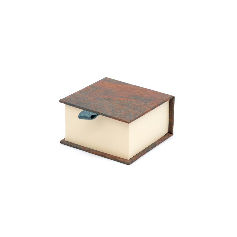 May include: A small, rectangular box with a brown wood-grain pattern on the lid and a light beige interior. The box has a blue ribbon pull.