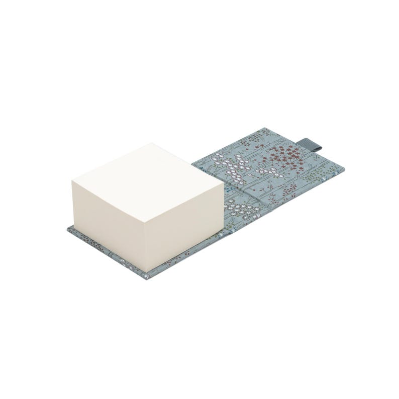 Op de afbeelding: Een grijs en wit gepatroneerd notitieboekje met een stapel witte plakbriefjes. Het notitieboekje heeft een bloemmotief met kleine rode bloemen.