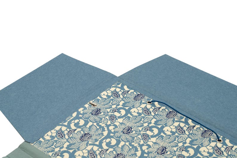Handgefertigte Sammelmappe mit Japanpapier bezogen und mit strapazierfähigem Bucheinbandgewebe eingefasst. Im Inneren schützen drei eingearbeitete Klappen den Inhalt zuverlässig vor dem Herausfallen. Ein Gummizugband hält die Mappe sicher verschlossen. Ideal für Zeichnungen, Dokumente, Briefe und andere kreative Arbeiten. Es besteht die Möglichkeit zur Personalisierung.