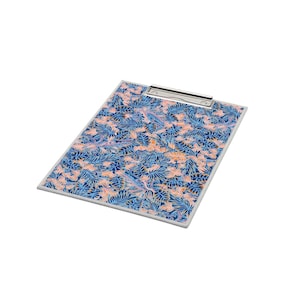 May include: A rectangular clipboard featuring a dense, repeating pattern of dark blue and light blue tropical leaves interspersed with soft peach-colored floral elements. The board includes a silver-toned metal clip at the top edge.