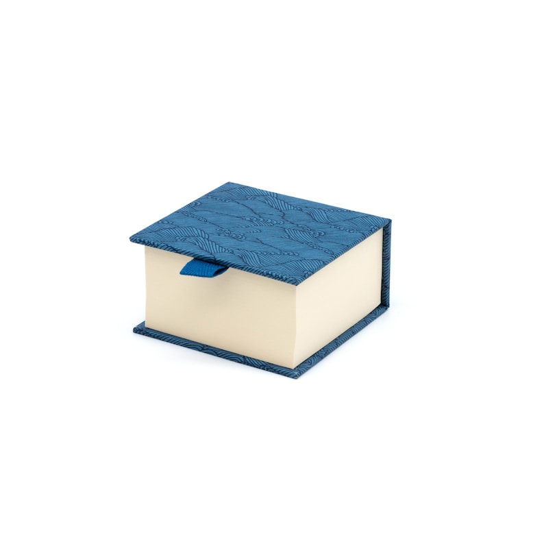 Puede incluir: Una peque&ntilde;a caja azul con un patr&oacute;n de ondas y una cinta azul. La caja est&aacute; cerrada y tiene un interior de color crema.
