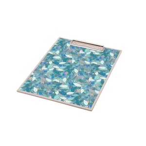 May include: A rectangular clipboard featuring a repeating pattern of leaves in various shades of blue, teal, and light green on a grey background. The board has a silver metal clip at the top center and a light grey border around the entire edge.