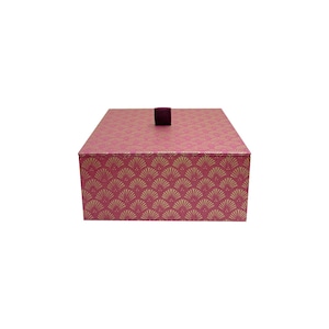 May include: A pink rectangular box with a gold fan design. It features a small, dark purple fabric loop on the lid. The box is likely for storage or gifting.