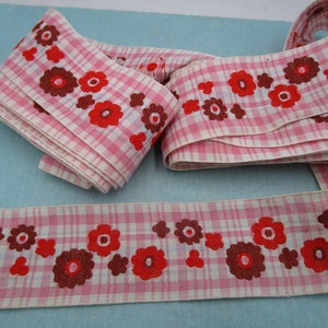 Könnte beinhalten: Rosa-weißes Vichy-Band mit Blumenmuster. Das Band hat ein sich wiederholendes Design aus roten und braunen Blumen. Das Band ist gefaltet und liegt auf einer hellblauen Oberfläche.