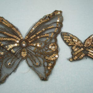 Könnte beinhalten: Zwei goldene Pailletten-Schmetterlingsapplikationen. Der größere Schmetterling ist etwa 10 cm breit und der kleinere etwa 5 cm breit.